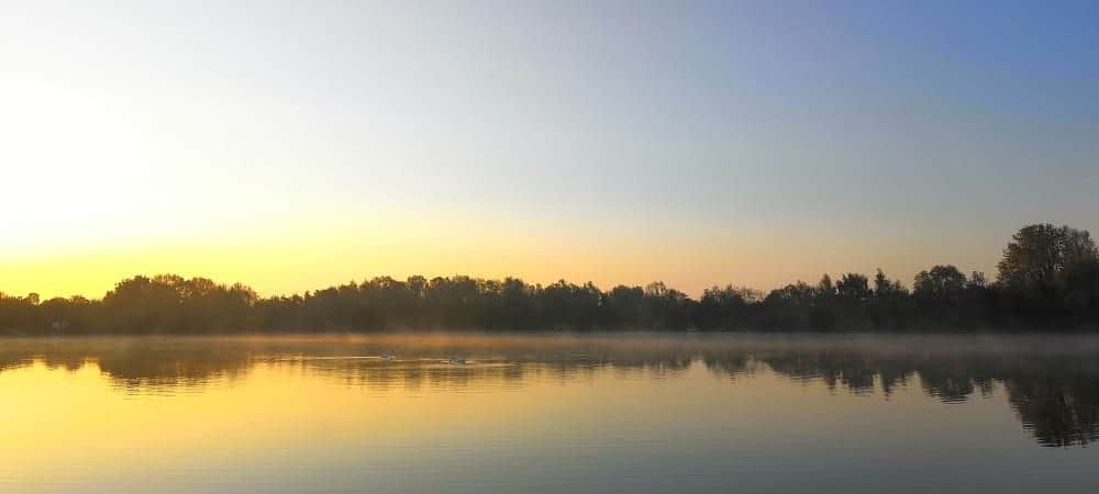 Serene sunrise over a calm lake with mist, perfect for fishing and outdoor activities at Carp Tax.